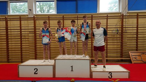 Chłopcy w wieku szkolnym wraz z trenerem pozują na podium trzymając medale i dyplomy. - Chłopcy w wieku szkolnym wraz z trenerem pozują na podium trzymając medale i dyplomy. Chłopcy w wieku szkolnym wraz z trenerem pozują na podium trzymając medale i dyplomy.