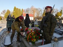 Cmentarz. Przy grobie weteranów powstania Wielkopolskiego stoi warta honorowa. Na pierwszym planie żołnierz na baczność z karabinem i bagnetem. Na grobie kwiaty. Drugi żołnierz stawia na grobie zapalony znicz. W tle widzać tablicę grobową na napisem Rodzina Walczaków.