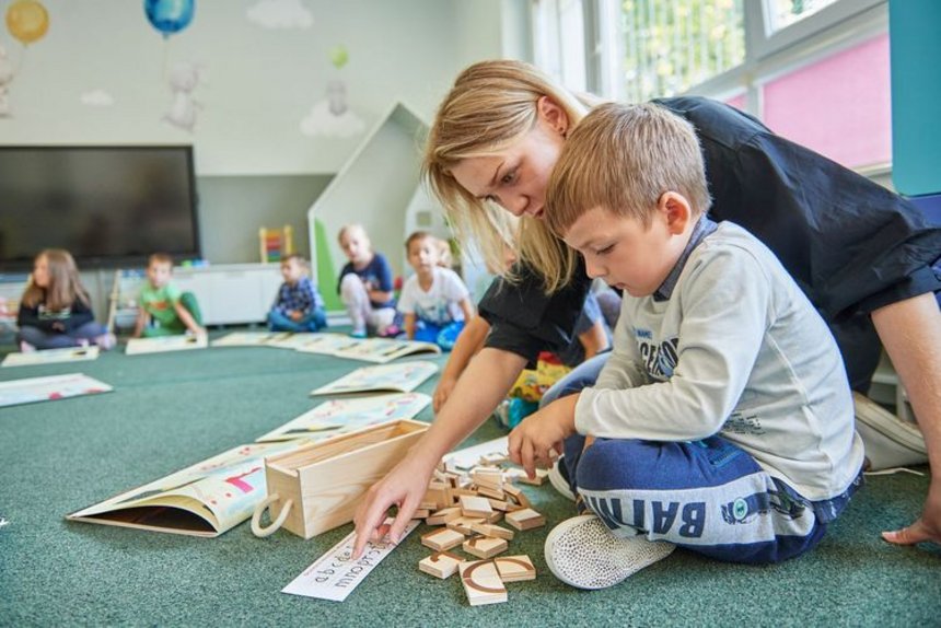 Dziecko w wieku przedszkolnym bawi się na dywanie podczas zajęć edukacyjnych.