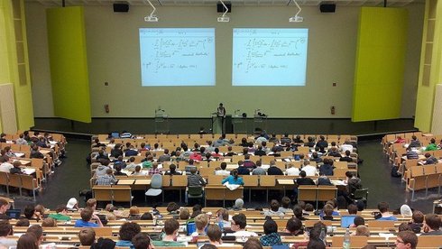 - sala wykładowa - aula wypełniona studentami siedzącymi przy długich stołach, w centrum katedra z wykładowcą i wyświetlona na dwóch ekranach ściennych prezentacja sala wykładowa - aula wypełniona studentami siedzącymi przy długich stołach, w centrum katedra z wykładowcą i wyświetlona na dwóch ekranach ściennych prezentacja
