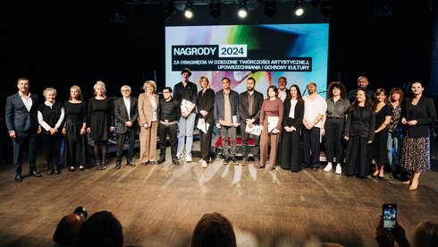 Na zdjęciu grupa osób, stojąca na scenie. Laureaci nagrody stoją w rzędzie na wprost. Ponad nimi napis: Nagrody 2024 za osiągnięcia w dziedzinie twórczości artystycznej, upowszechniania i ochrony kultury.