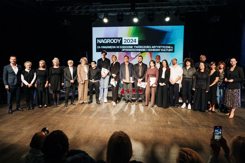 Na zdjęciu grupa osób, stojąca na scenie. Laureaci nagrody stoją w rzędzie na wprost. Ponad nimi napis: Nagrody 2024 za osiągnięcia w dziedzinie twórczości artystycznej, upowszechniania i ochrony kultury.